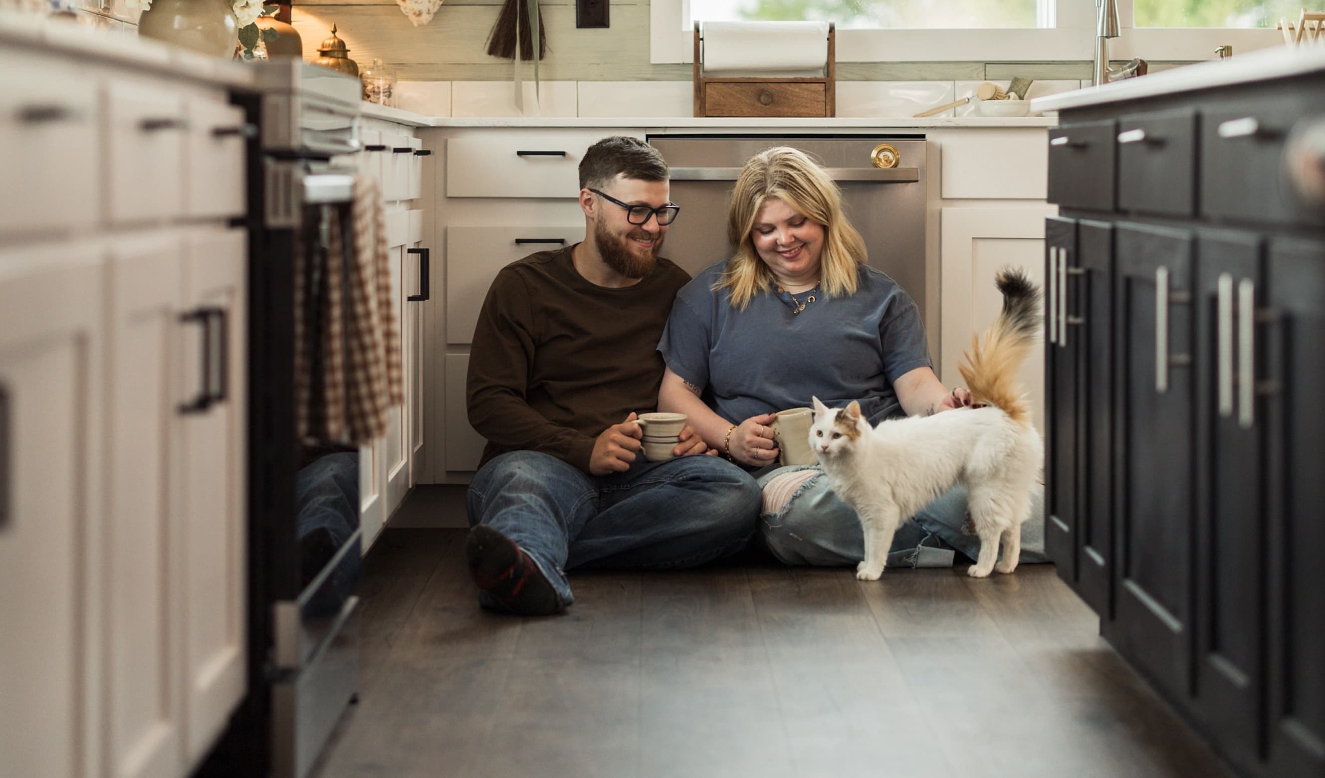 A couple sits on their kitchen floor with their dog.