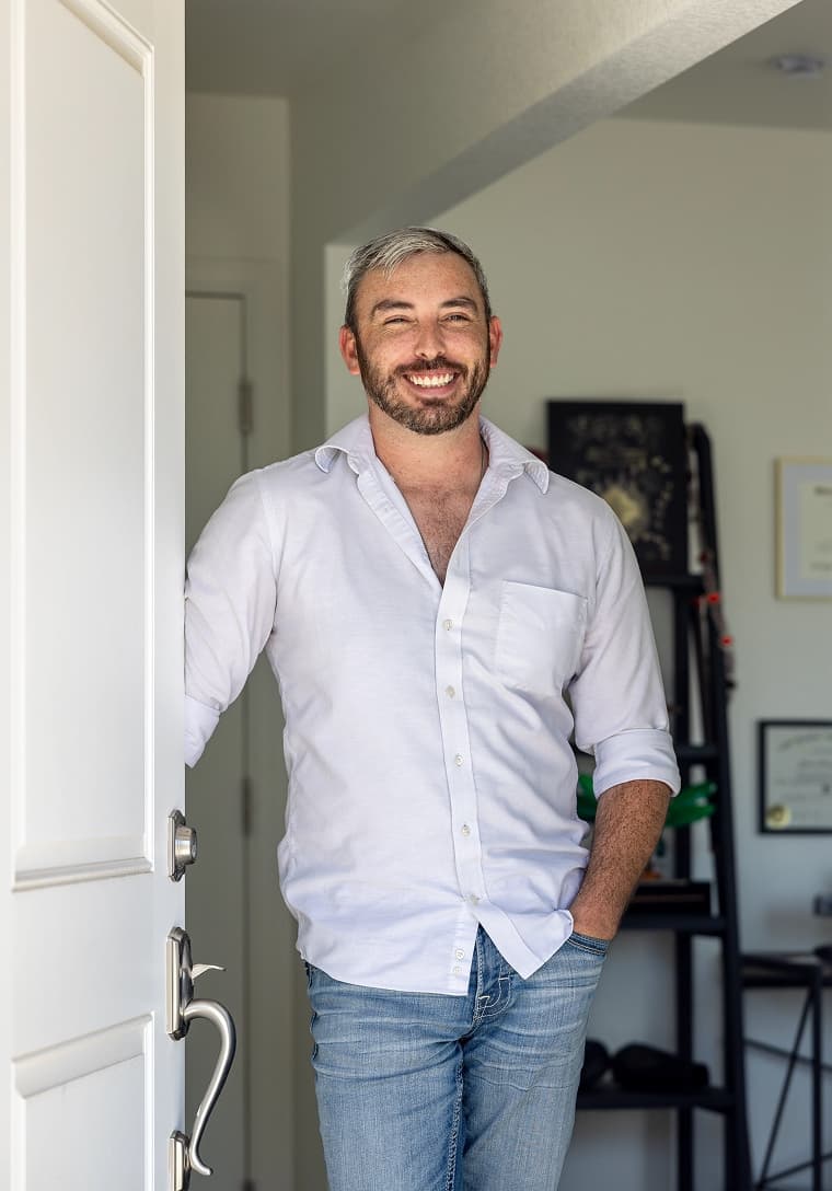 A smiling man leaning in the open front doorway of his home.