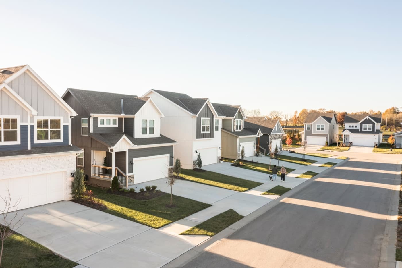 A row of two-story homes along a neighborhood street with a couple walking their dog.