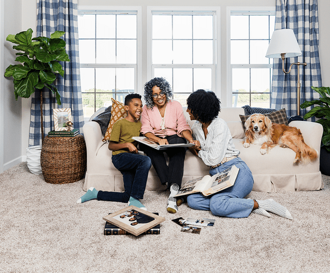A family looks through photo albums together on the couch of their Clayton home, with their dog resting beside them.