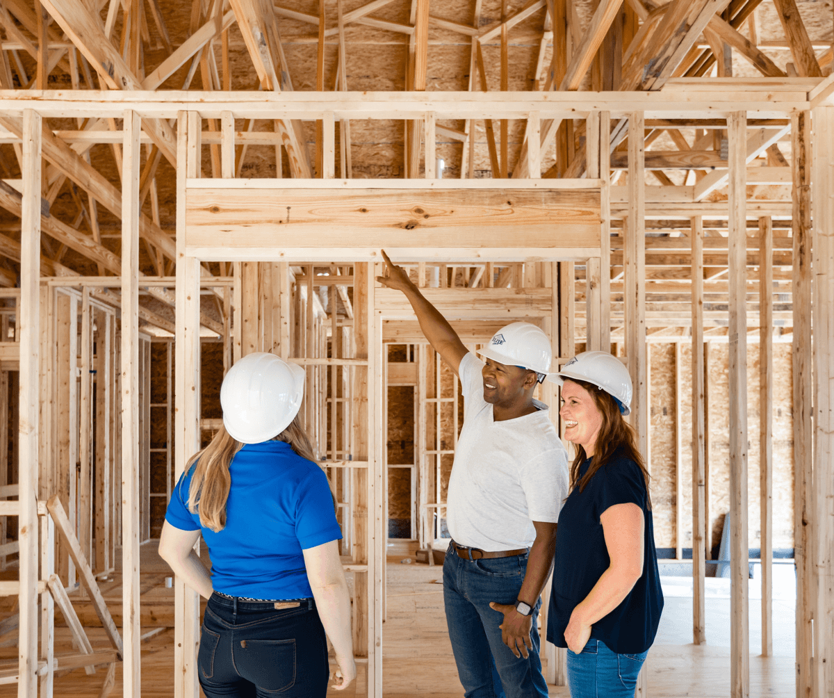 Three Clayton team members in hard hats inspecting the wood framing inside a new home under construction.