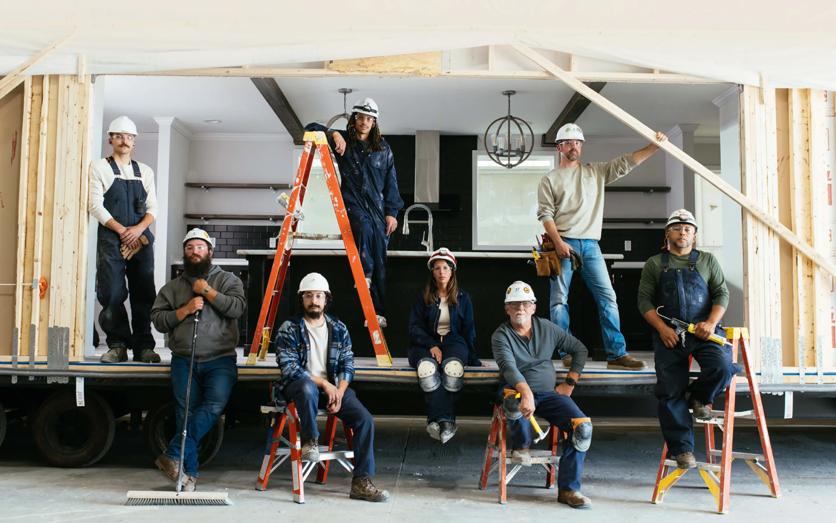 Clayton builders stand together beside a modern manufactured home under construction at a building facility.