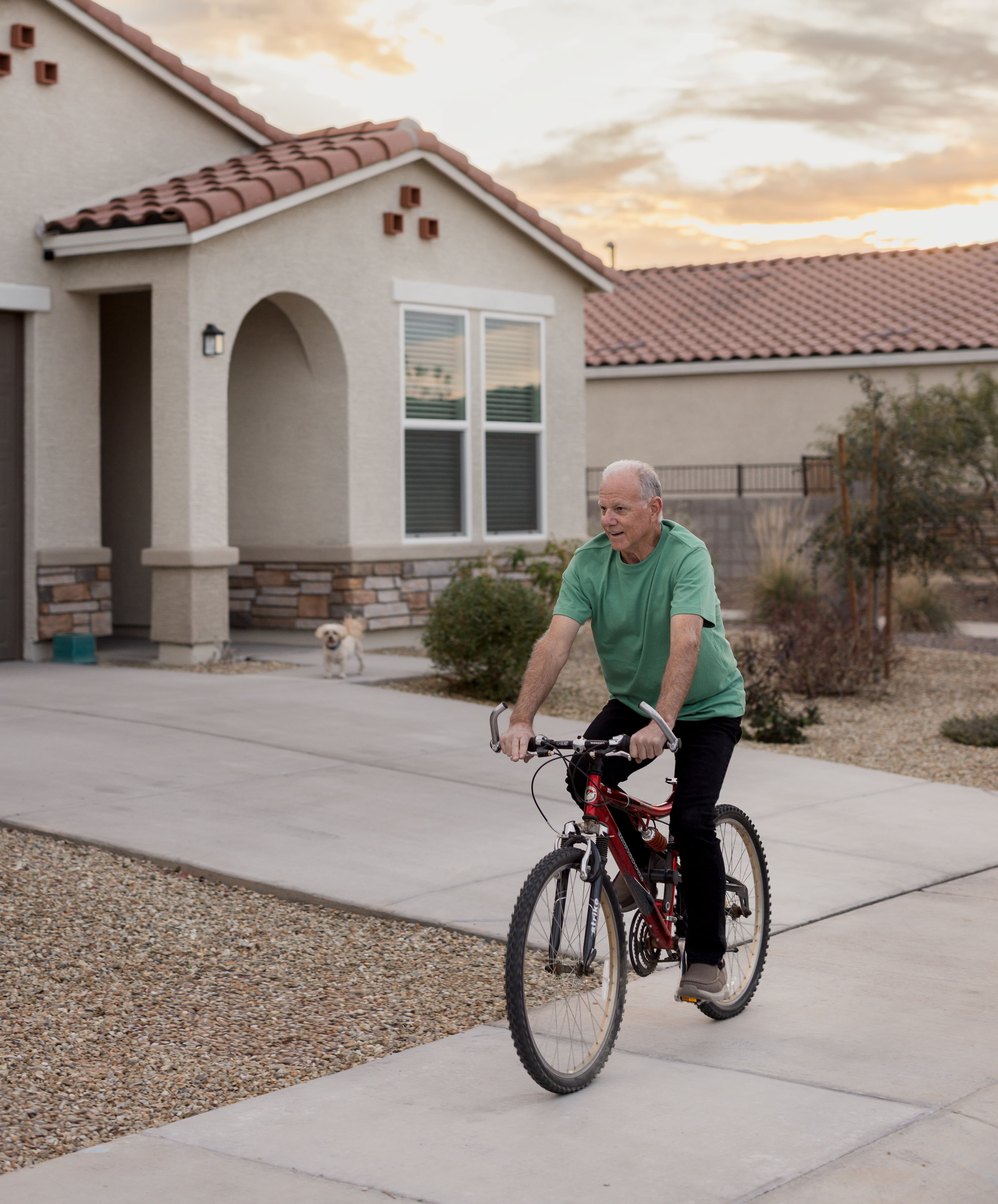 Don rides his bike outside his new construction site built home by Clayton as his little white dog supervises.