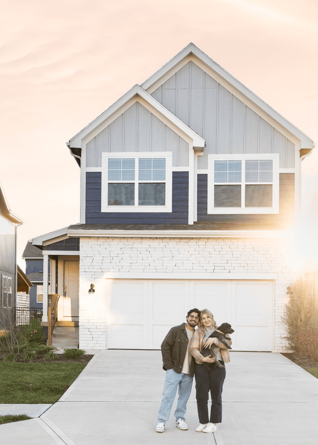 A couple stands outside their two-story new construction home with their dog.