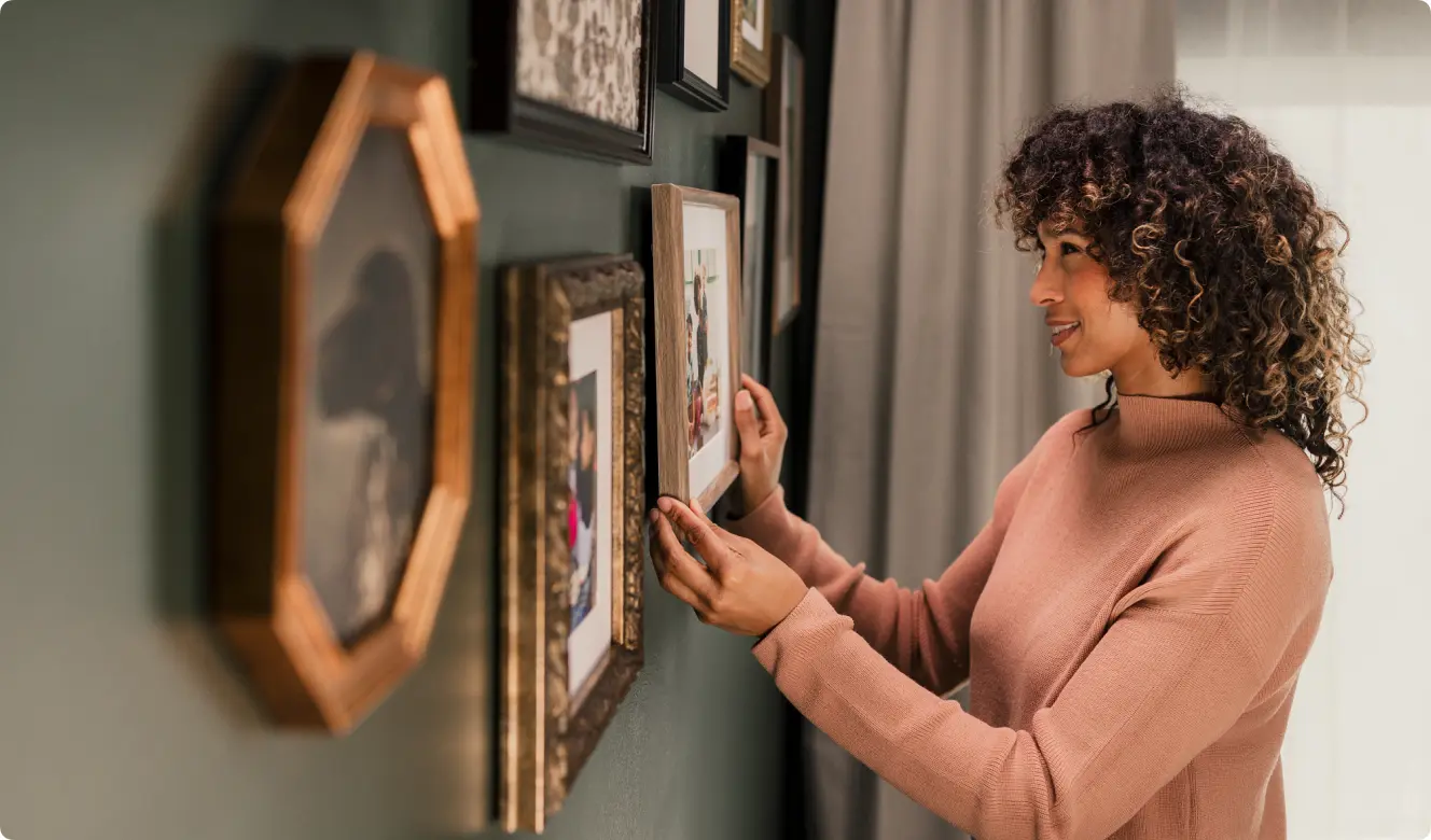 A woman hangs pictures in frames on a green wall inside her modern manufactured home.