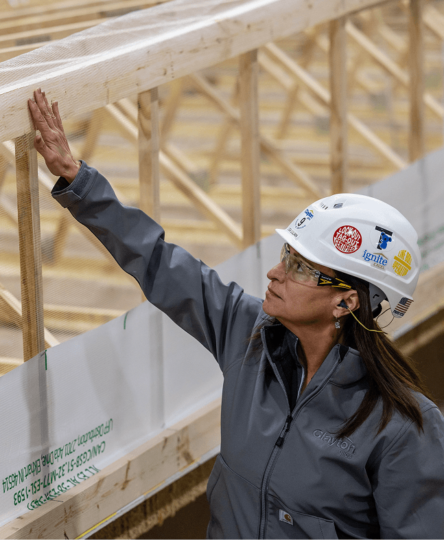 A Clayton team member in a hard hat inspecting wooden roof trusses inside a building facility.