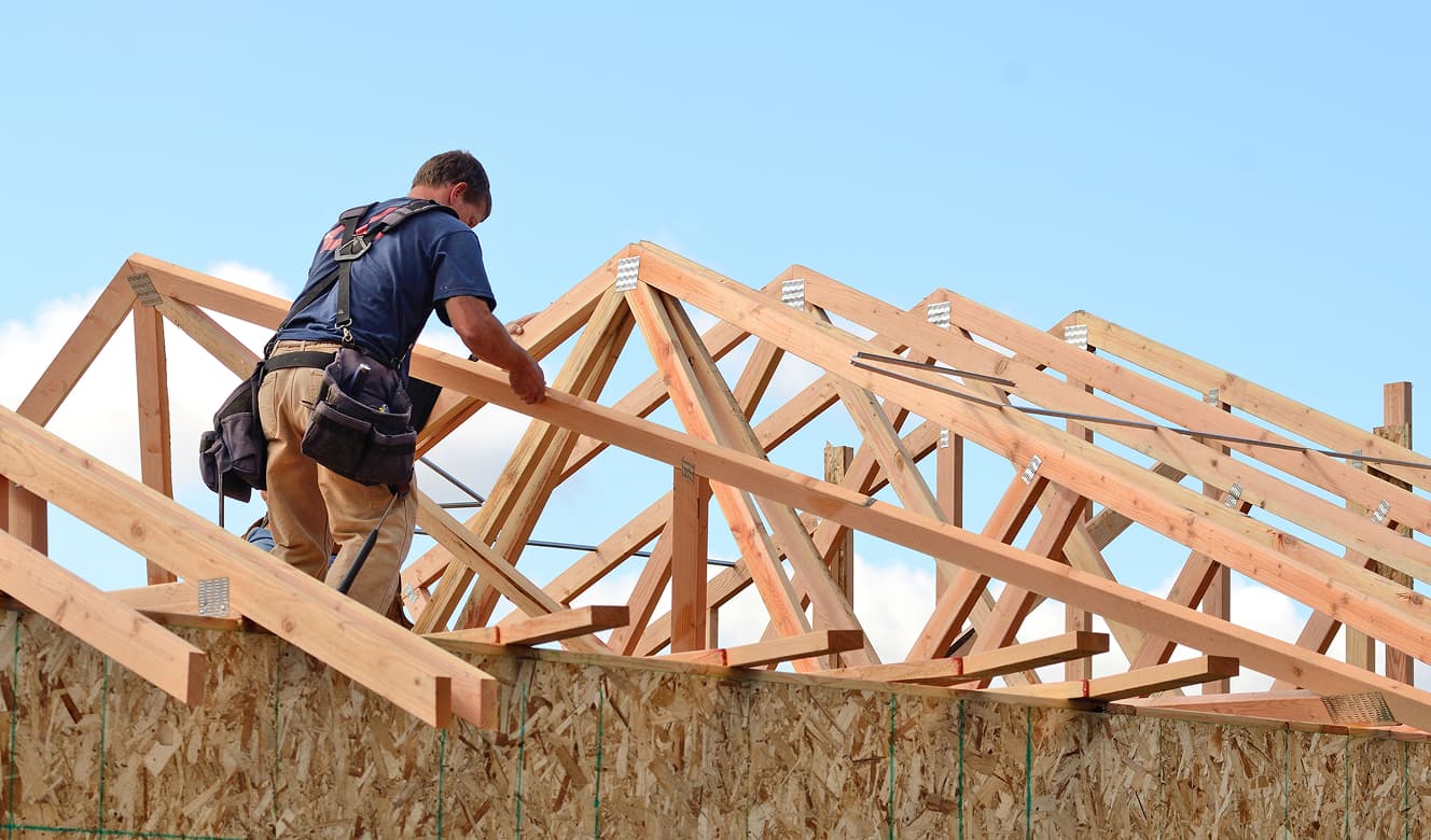 A builder secures wooden roof trusses on top of a new construction home.