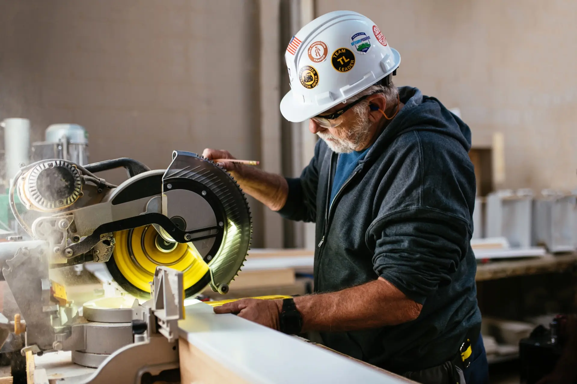 A worker in a hard hat operates a miter saw inside a Clayton home-building facility.