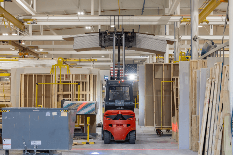 A red electric forklift moving building materials inside a climate-controlled facility.