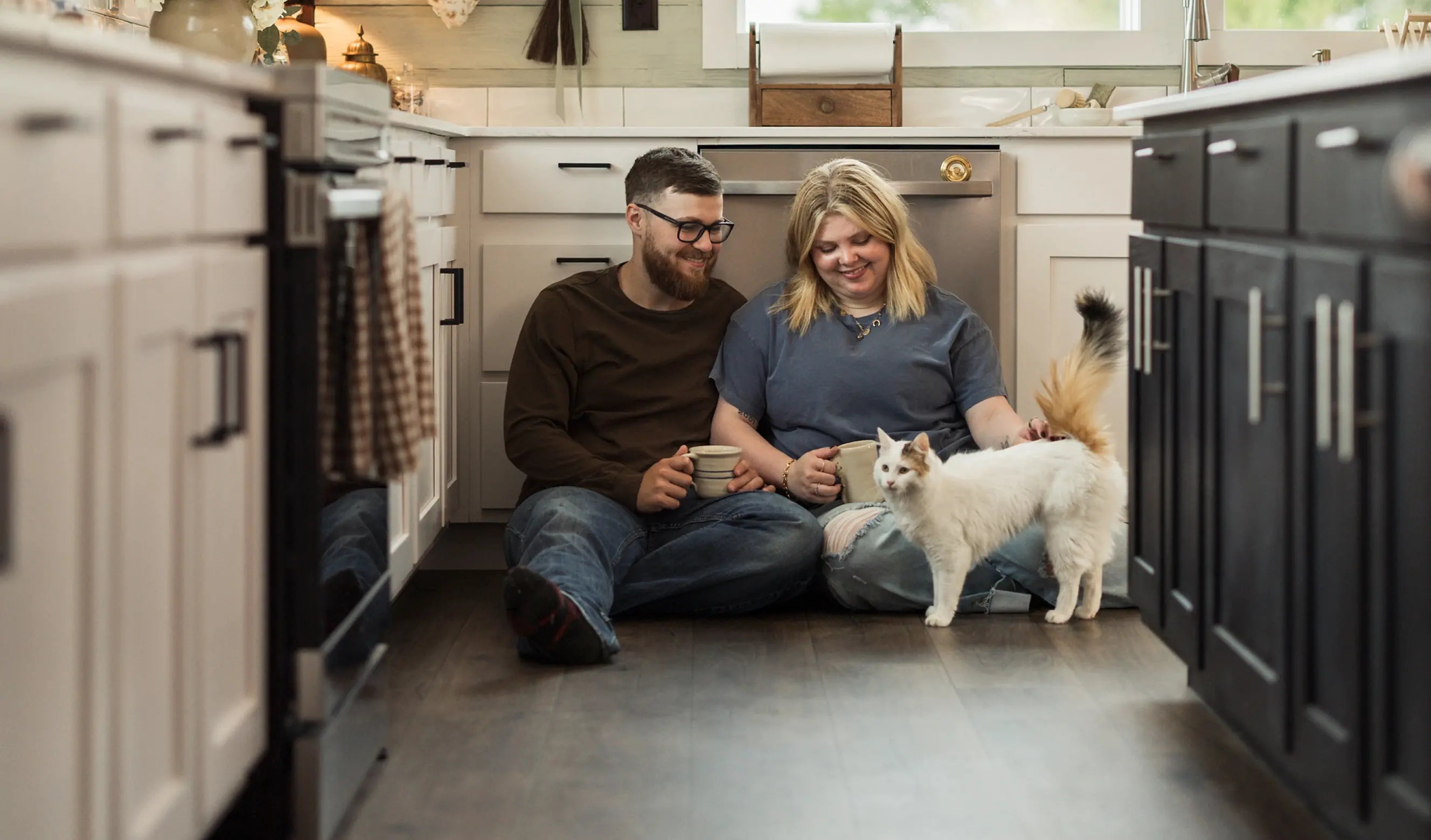 A couple sits on their kitchen floor with their dog.